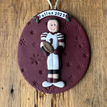 Load image into Gallery viewer, Decorative ornament with a person holding a football on a purple round base, hanging on a wooden surface.
