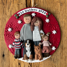 Load image into Gallery viewer, Personalized family ornament with four people and two dogs on a red background, hanging on a wooden surface.

